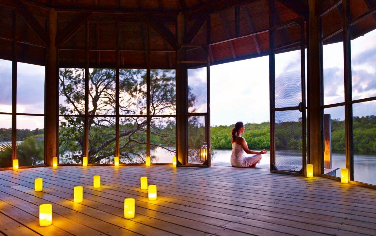 Woman meditating on wooden deck with candles and lake view